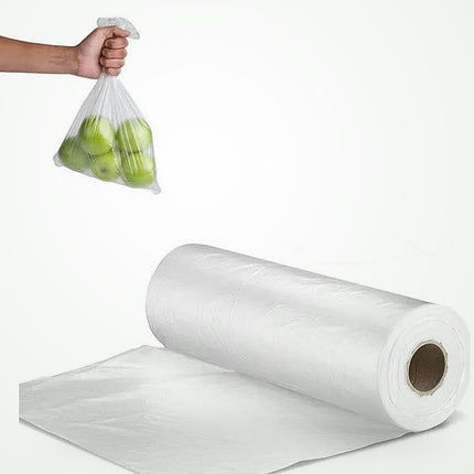 A roll of clear plastic bags with a strip peeled, shown on a white background with a hand holding a clear plastic bag filled with green apples in the upper left.